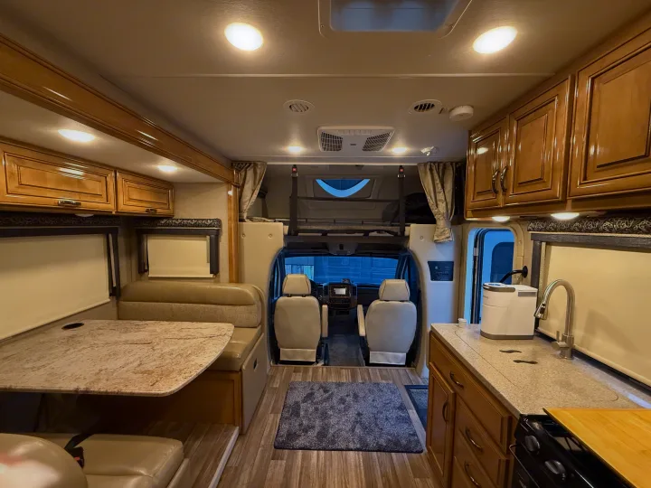 This inviting RV rental interior features a dining booth, kitchen, and overhead bunk, offering comfortable travel accommodations.. Thor Quantum 2018