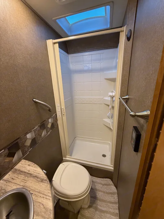 Clean RV rental bathroom features a compact shower, toilet, sink, and skylight, perfect for travel.. Thor Quantum 2018