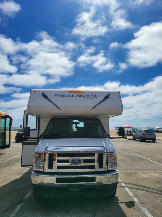 White Ford Frelander by Coachmen RV rental parked on a sunny day at a beachside lot, with blue sky and clouds.. Forest River Coachmen Freelander 2021