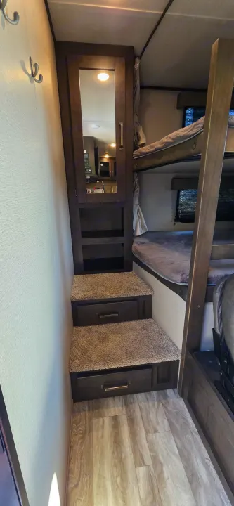 Efficient RV rental design: bunk beds, built-in storage stairs, and kitchen area reflected in a mirrored cabinet. Smart storage.. Grand Design Transcend Xplor 2021