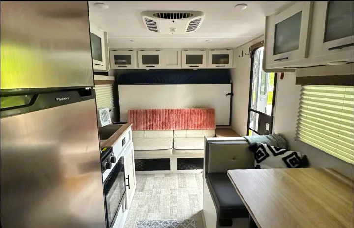 Inside a bright rv rental: kitchen (Furrion fridge/stove), convertible sofa/bed, and dinette offer a comfy space.. Forest River No Bounderies 2024