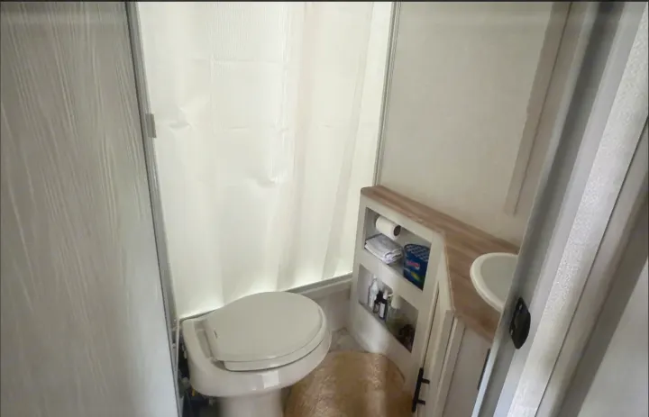 RV rental bathroom: compact toilet, white shower curtain, sink, and built-in storage for essentials.. Forest River No Bounderies 2024