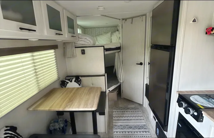 RV rental interior features a dining area, cozy bunk beds, and kitchen with fridge, stove, and overhead cabinets.. Forest River No Bounderies 2024