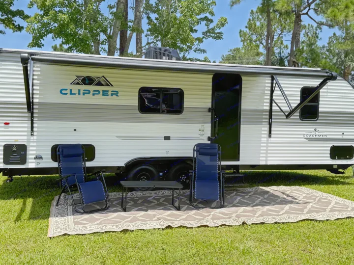 Enjoying an RV rental: a Coachmen Clipper travel trailer with an extended awning, chairs, & rug on green grass.. Coachmen Clipper 25BH 2025
