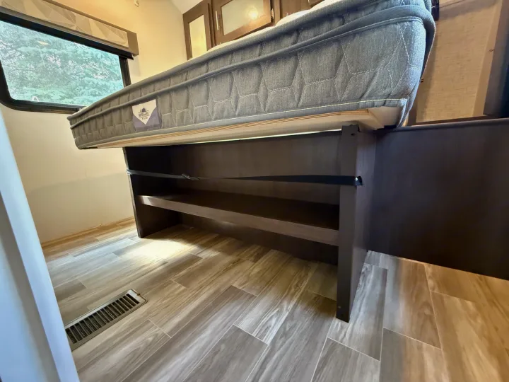 RV rental interior: A mattress is propped up, revealing shelves and storage below. Features a large window and wood-look floor.. Forest River Salem 2019