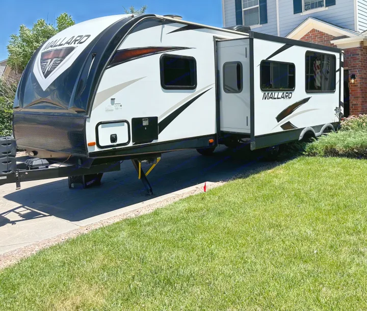White & black Mallard RV rental on a sunny driveway. This travel trailer's extended slide-out and design are perfect for trips.. Heartland RVs Mallard 2019