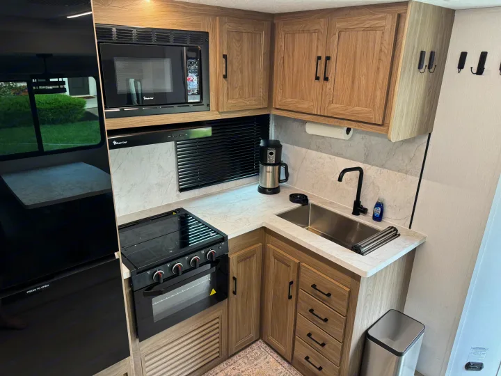 Modern RV rental kitchen with microwave, oven, sink, and black refrigerator. All set for travel adventures.. Coachmen Freedom Express Ultra Lite 2025
