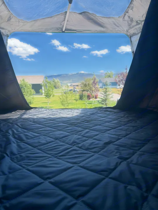 Inside an RV rental: a quilted sleeping area with a bright view of houses, trees, and mountains under a blue sky.. Forest River Nobo 10.7 2024