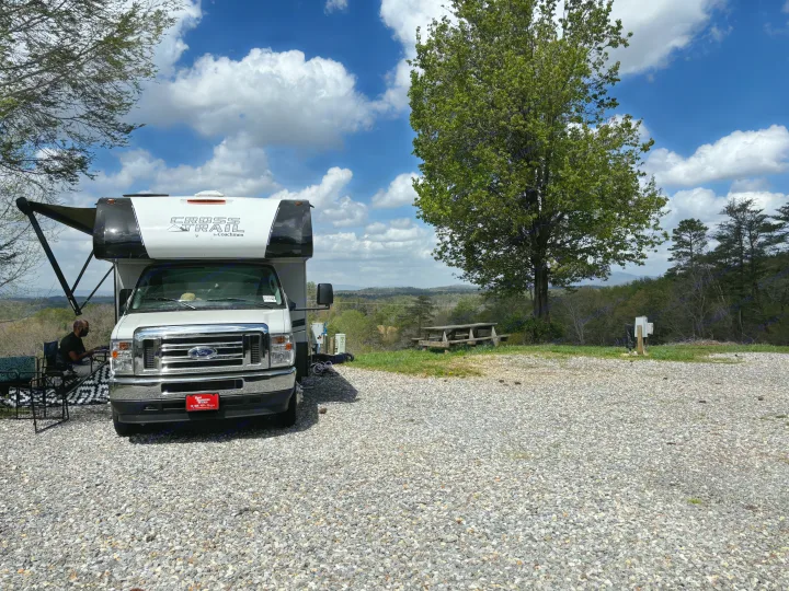 Scenic rv rental campsite: A Class C RV on gravel with a man relaxing, mountain backdrop & blue sky.. 1FDWE3FNXSDD14715 Cross trail 22xgf 2025