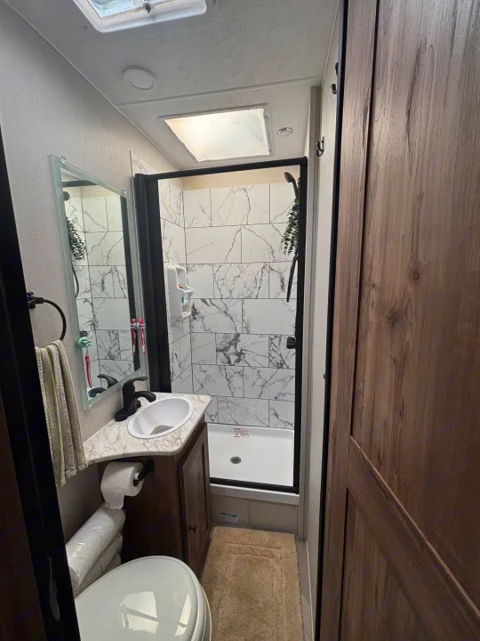 RV rental bathroom with a toilet, sink, mirror, and a shower featuring marble-look tiles, brightened by a skylight.. 1FDWE3FNXSDD14715 Cross trail 22xgf 2025