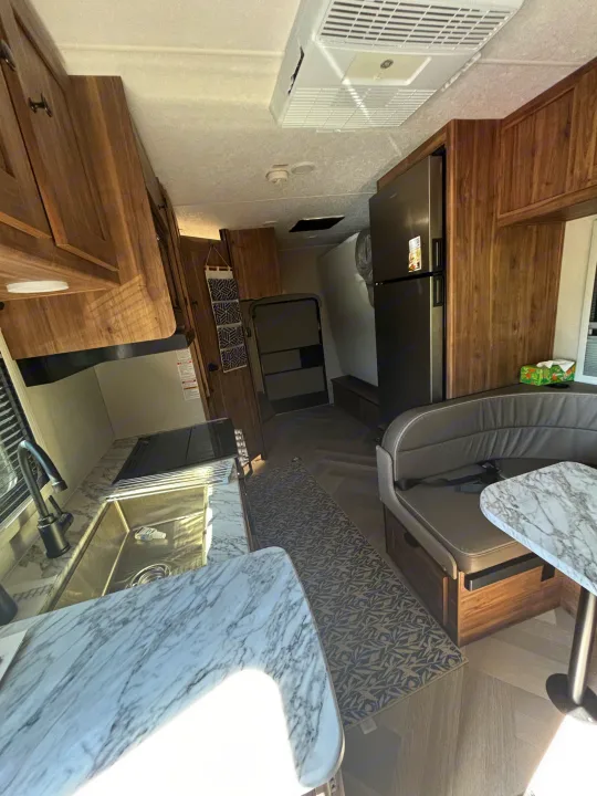 This RV rental interior showcases a compact kitchen with marble-look counters, wood cabinets, a dining booth, and a refrigerator.. 1FDWE3FNXSDD14715 Cross trail 22xgf 2025