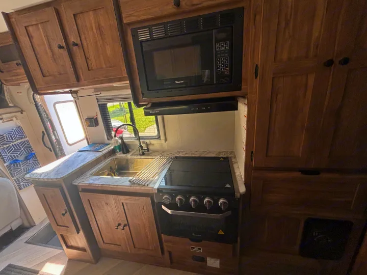 This RV rental features a compact kitchen with a sink, stovetop, microwave, and wooden cabinetry for your travels.. 1FDWE3FNXSDD14715 Cross trail 22xgf 2025