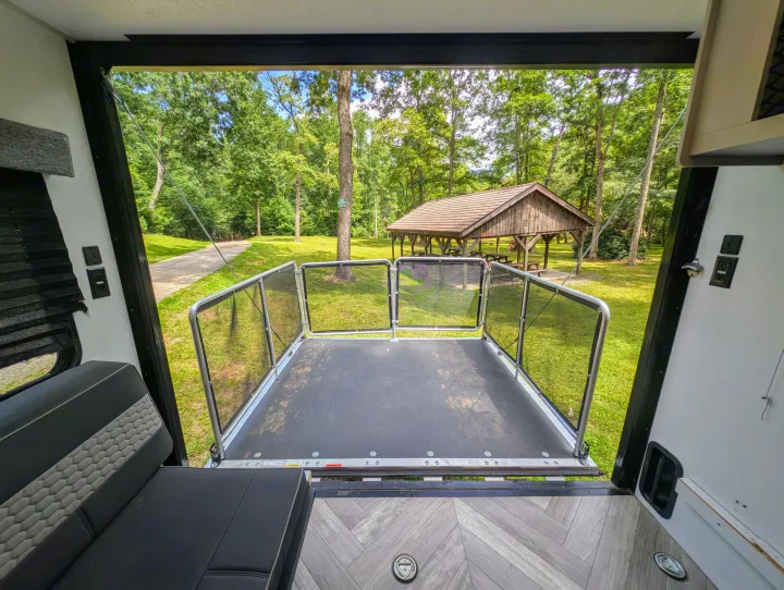 RV rental's spacious rear deck with safety railings, offering views of a serene forest and a picnic pavilion.. Forest River Salem 2021