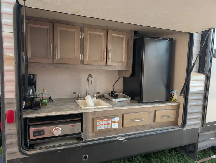 This RV rental outdoor kitchen features an Everchill fridge, sink, and Suburban griddle for convenient outdoor cooking & entertaining.. Forest River Coachmen Aurora 2022