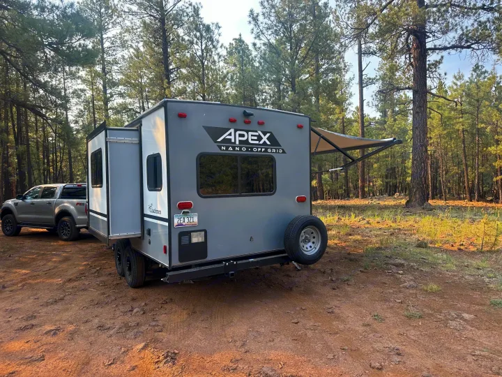 Grey Apex Nano RV rental and truck parked in a pine forest campsite. Perfect for off-grid camping.. Coachmen Apex Nano - Off Grid 2022