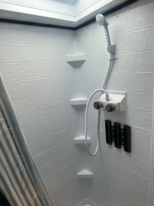 Inside an RV rental shower: a compact white space with handheld shower, dual water knobs, and mounted storage. Functional travel bathroom.. Coachmen Apex Nano - Off Grid 2022