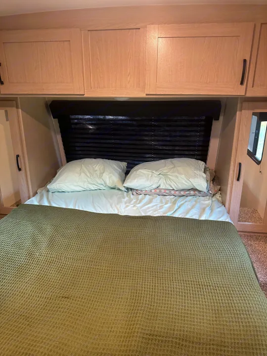 Inside an RV rental: a compact bedroom features light wood cabinets, a bed with light blue sheets, and a green blanket.. Coachmen Apex Nano - Off Grid 2022