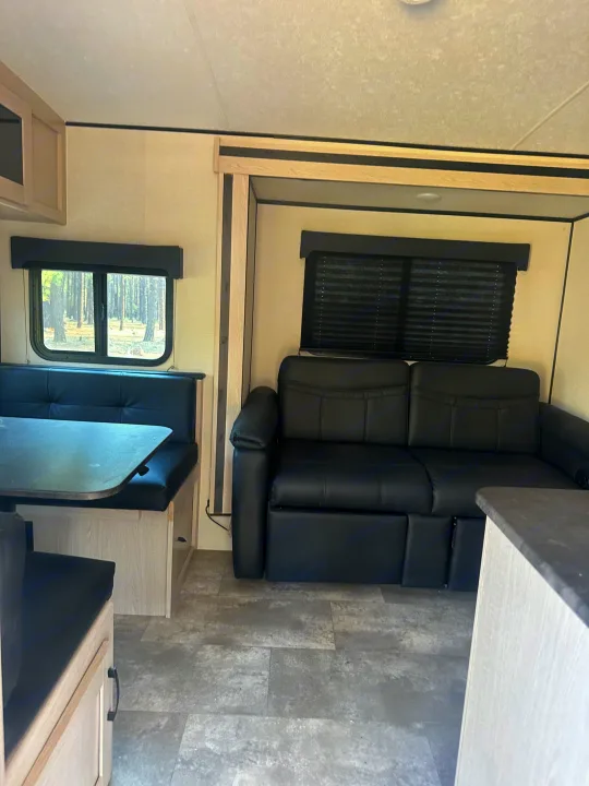 Inside this RV rental: modern interior with dinette, black sofa, and large forest-view window.. Coachmen Apex Nano - Off Grid 2022