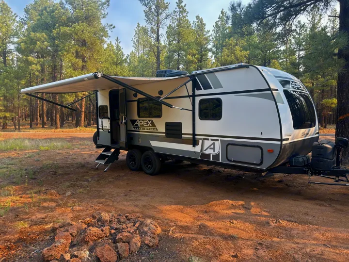 This Apex Nano Off Grid travel trailer (RV rental) is set up with its awning out in a peaceful pine forest campsite.. Coachmen Apex Nano - Off Grid 2022