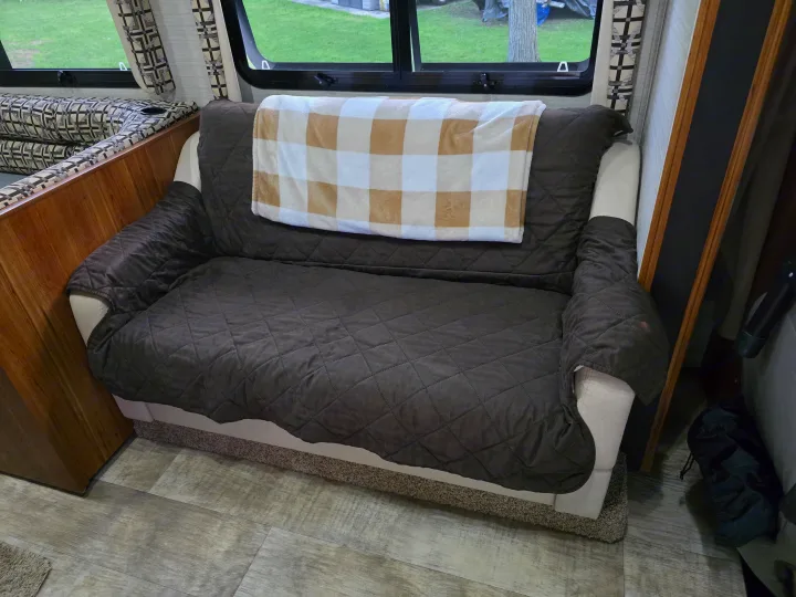 Cozy RV rental interior shows a brown sofa with a plaid blanket, window view, and dinette seating.. Jayco Redhawk 2017