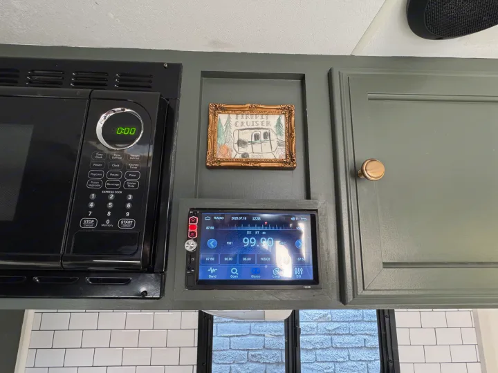 RV rental interior: A functional kitchenette with microwave, modern radio displaying 99.90 MHz, and olive green cabinets.. Sportsmen Classic 2014