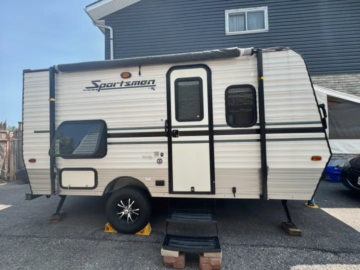 White Sportsmen by KZ travel trailer, an RV rental, parked with leveling jacks & wheel chocks on asphalt.. Sportsmen Classic 2014