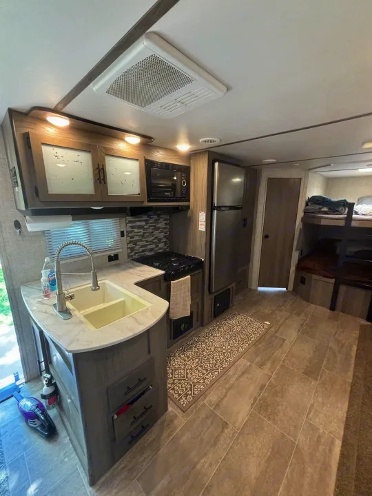 Spacious RV rental interior featuring a modern kitchen with sink, stove, microwave, and fridge, plus bunk beds.. Gulf Stream Ameri-Lite 2021