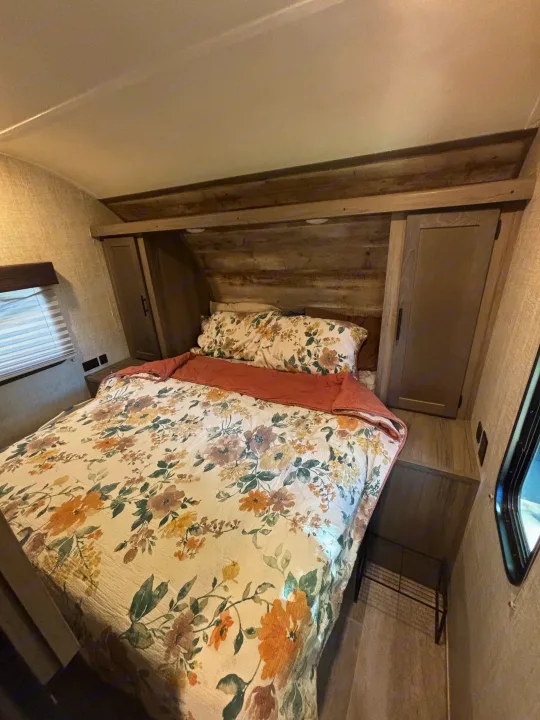 Cozy RV rental bedroom featuring floral bedding, built-in storage, and warm wood accents for a comfortable stay.. Gulf Stream Ameri-Lite 2021