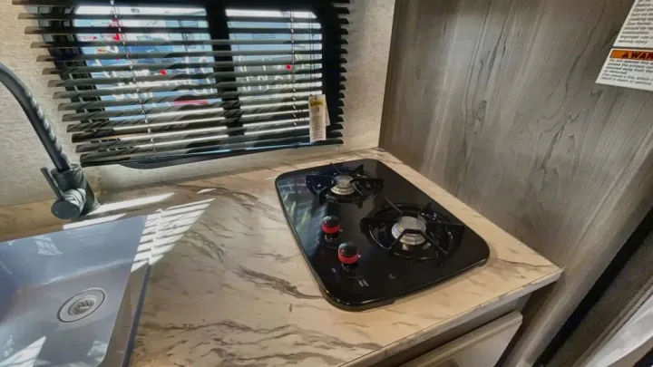 Compact RV rental kitchen with sink, faucet, and two-burner cooktop on a marble-look counter.. Keystone RV Hideout Sport 2024