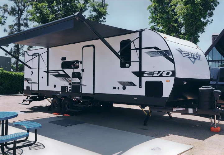 Spacious white EVO travel trailer RV rental with a deployed black awning at a sunny campsite, ready for adventure.. Forest River Evo CSJT2650G 2023