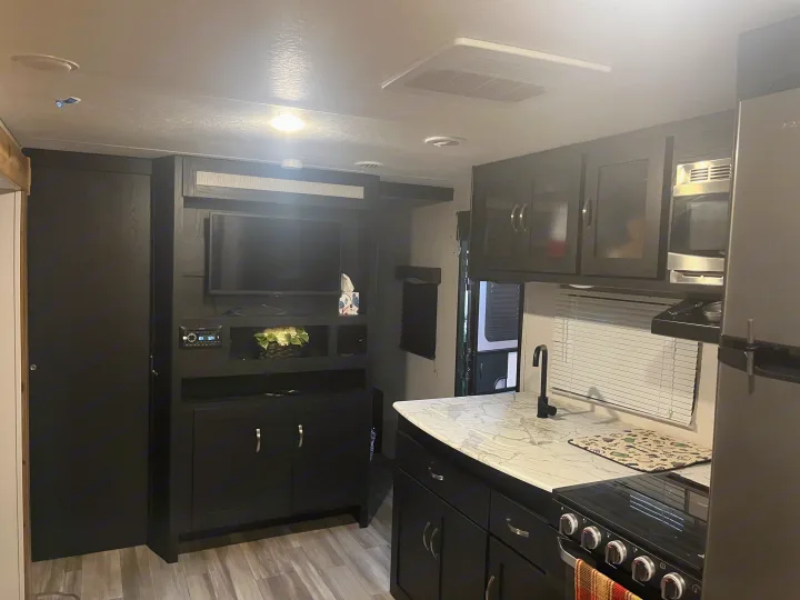 Sleek RV rental interior featuring a modern kitchen with appliances, an entertainment center with TV, and dark cabinetry.. Coachmen 29SE 2022