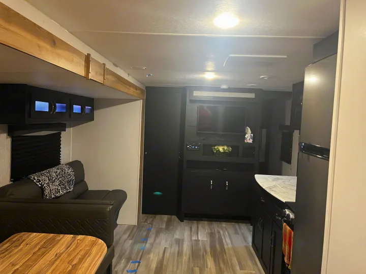 Spacious RV rental interior featuring a modern living area with a dark entertainment center, couch, and compact kitchen.. Coachmen 29SE 2022