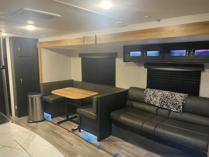 An RV rental interior with a dark U-shaped dinette, sofa, and clean wood-look flooring in the main living space.. Coachmen 29SE 2022