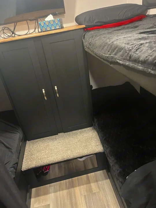 Inside an RV rental: black storage cabinet, upper & lower bunk beds with cozy bedding, and a TV setup.. Coachmen 29SE 2022