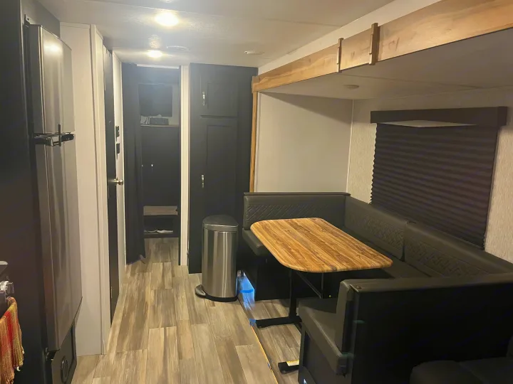 Modern RV rental interior: U-shaped dinette with wood table, stainless fridge, and a bright hallway view.. Coachmen 29SE 2022