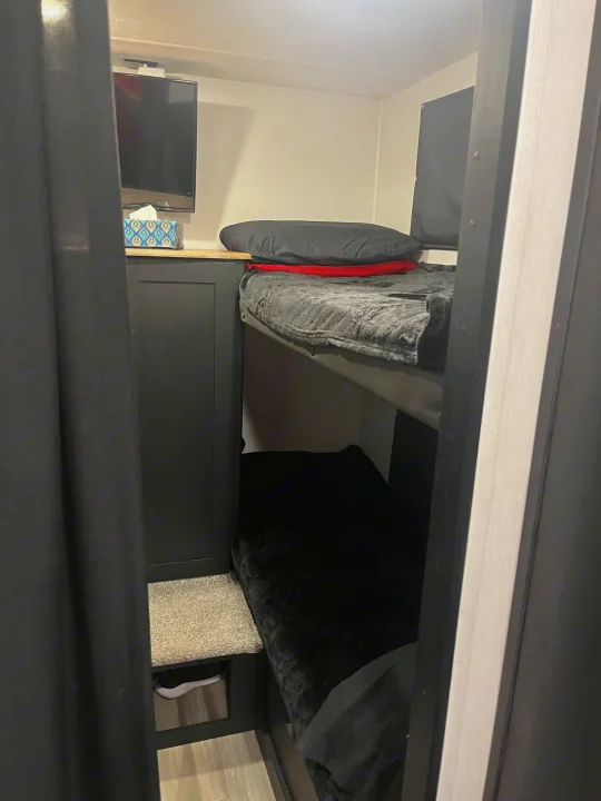 Inside an RV rental: cozy bunk beds with dark bedding, a TV, and integrated storage, maximizing compact space.. Coachmen 29SE 2022