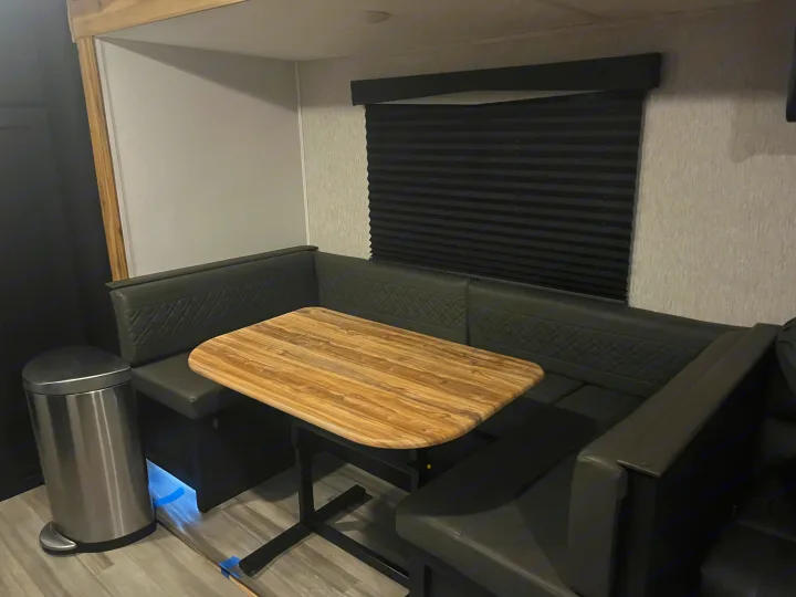 Spacious RV rental dinette: comfy dark U-shaped booth seating, light wood-grain table, and window blind, ideal for travel.. Coachmen 29SE 2022