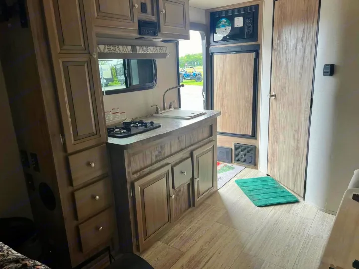 Inside an RV rental: a compact kitchen with a stove, sink, refrigerator, microwave, and wood-look cabinets.. Palomino Real Lite 2019