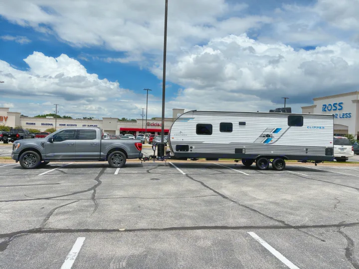 Gray Ford F-150 towing a Coachmen Clipper RV rental in a retail parking lot, with stores and cloudy sky.. Coachmen 25QBH 2025