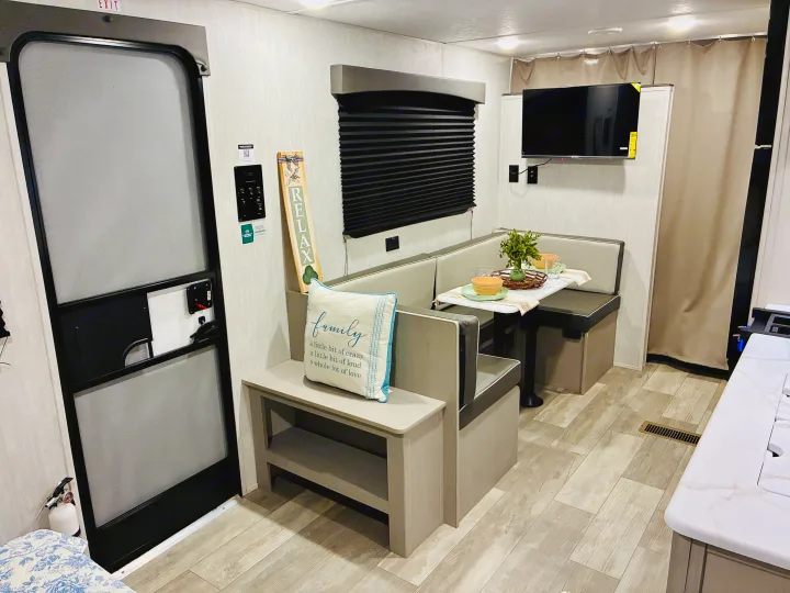 RV rental interior: a cozy dinette with a table, adjacent kitchen counter, and a prominent exit door.. Coachmen 25QBH 2025