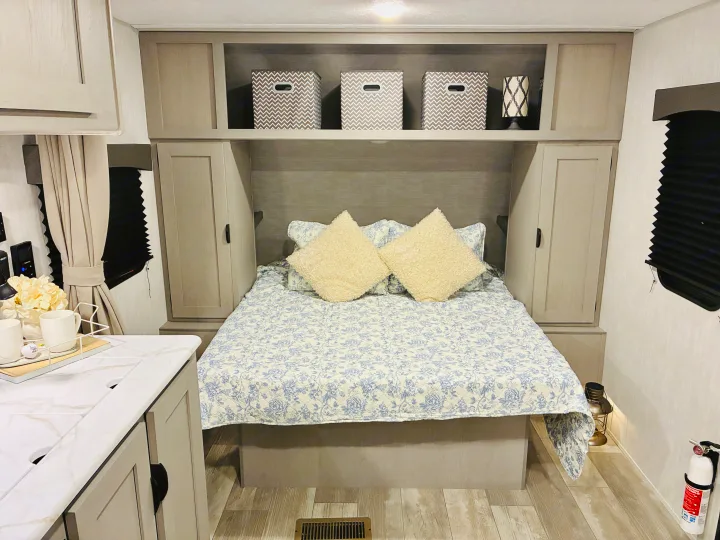 Bright RV rental bedroom: cozy bed with floral quilt, ample built-in storage, and light wood flooring.. Coachmen 25QBH 2025