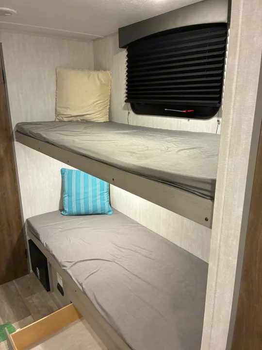RV rental: Compact sleeping area with two bunk beds, fitted with grey sheets and pillows. Features window and under-bed storage.. Coachmen 25QBH 2025