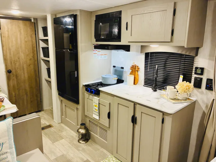 Explore the compact kitchen of an RV rental, complete with a stove, microwave, fridge, sink, and storage options.. Coachmen 25QBH 2025