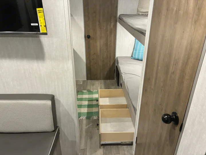 Spacious RV rental interior featuring cozy bunk beds with pull-out storage steps, a TV, and comfortable living space.. Coachmen 25QBH 2025