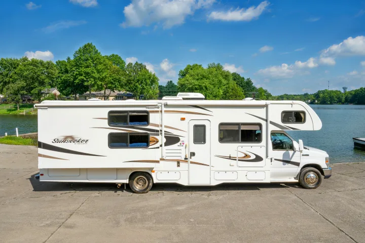 White Sunseeker by Forest River RV rental parked by a serene lake under a clear sky, perfect for outdoor adventures.. Forest River Sunseeker 2015