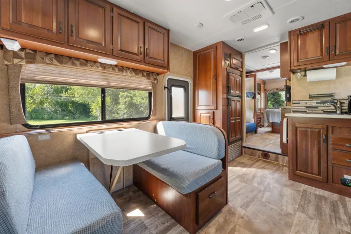 Spacious RV rental with a comfortable dinette, equipped kitchen, and large window offering scenic outdoor views.. Forest River Sunseeker 2015