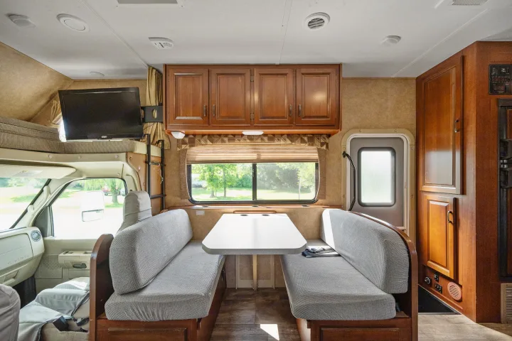 Spacious RV rental interior with a cozy dinette, overhead storage, and TV. Ideal for family road trip comfort.. Forest River Sunseeker 2015