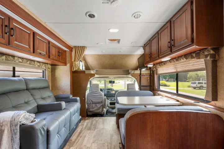 Spacious RV rental interior with a grey couch, dinette, and overhead cabinets; showing a comfortable living space.. Forest River Sunseeker 2015