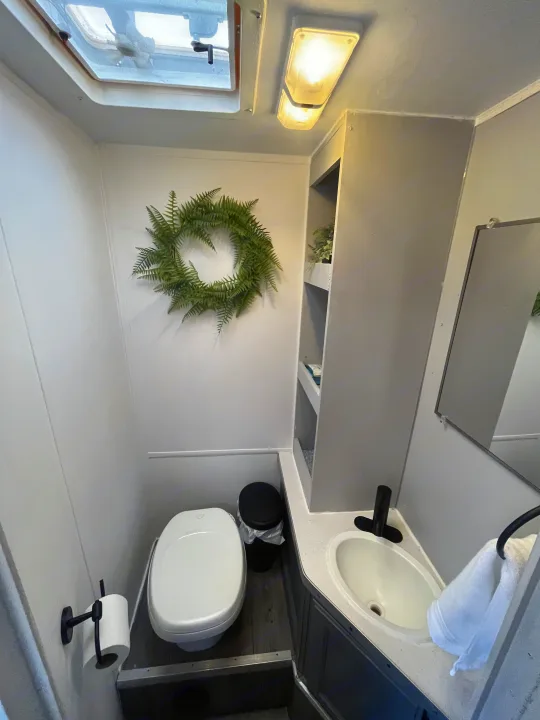 Well-lit RV rental bathroom with compact toilet, sink, mirror, and storage shelves. Features modern grey and white decor.. Gulf Stream Ultra 1998