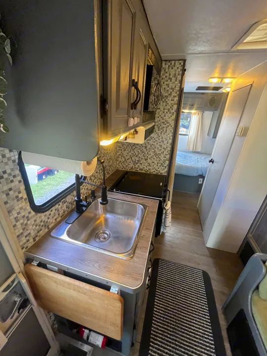 Step into this modern RV rental: a compact kitchen with a sink, stove, & mosaic backsplash, opening to a cozy bed.. Gulf Stream Ultra 1998